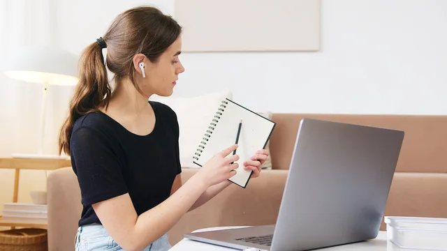 Concentrated young female student in earbuds showing notebook with notes during video conference distance learning concept. Automating webinar campaign operations